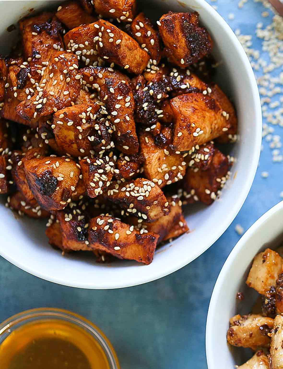 A white bowl filled with spicy Korean chicken and sprinkled with sesame seeds