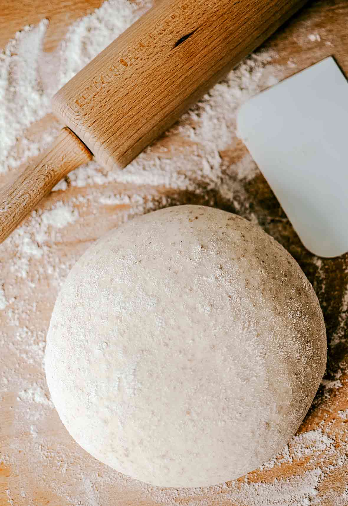 A ball of whole wheat pizza dough on a floured surface