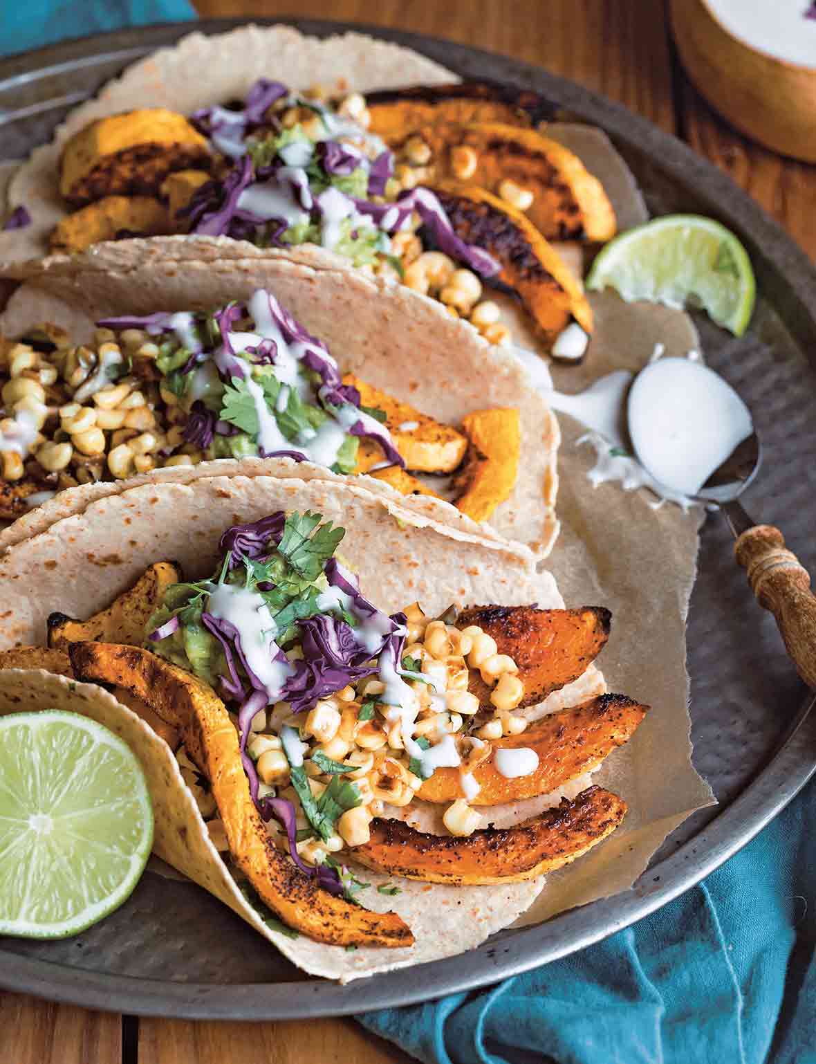 A platter of butternut squash tacos made with tortillas filled with strips of roasted squash, corn, cabbage, guacamole, and sour cream