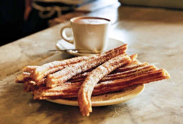 A plate of churros with a cup of hot chocolate in the background