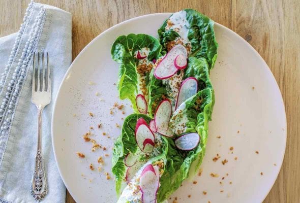 A white plate topped with Little Gem salad with bread crumb croutons, sliced radish, and buttermilk dressing