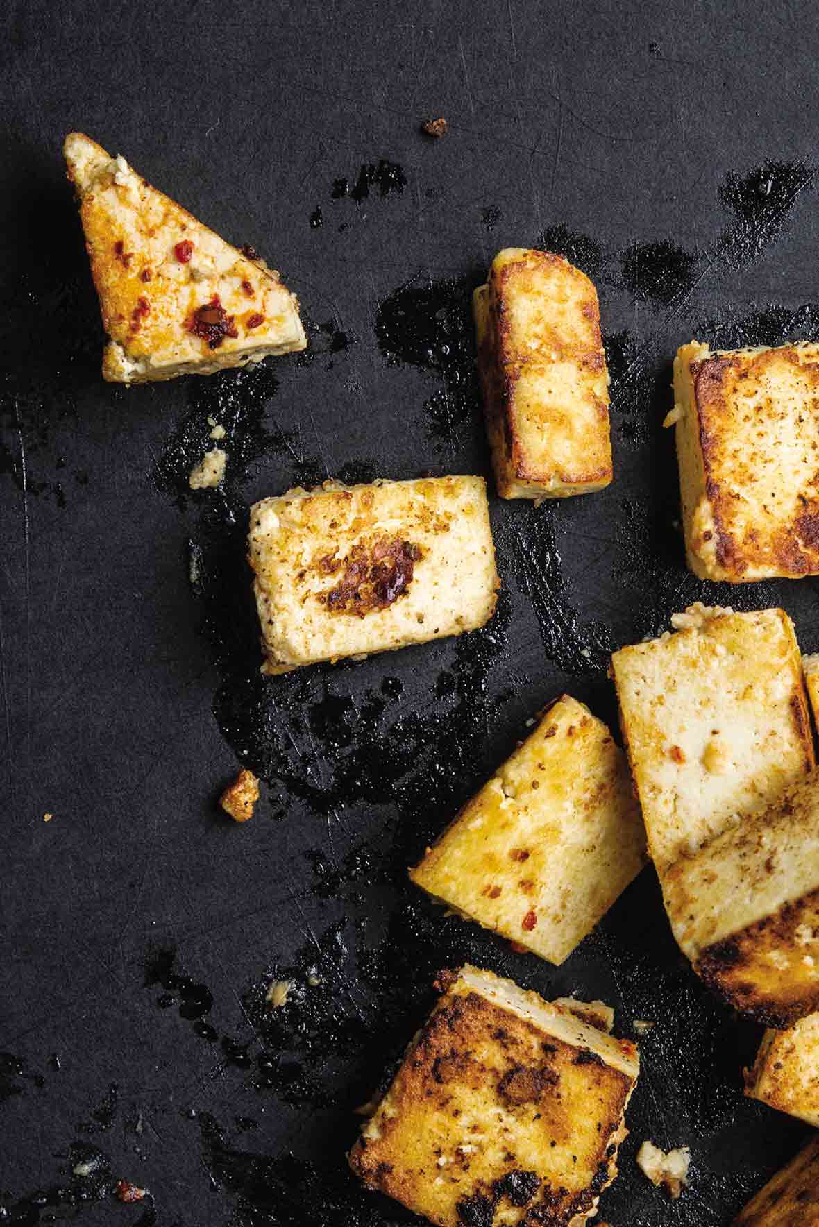 Several irregularly shaped pieces of miso glazed tofu on a black slate background