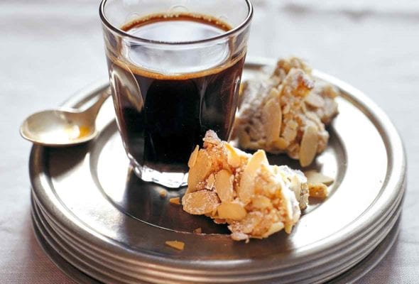Two pieces of Rosa's almond biscotti on a stack of plates with a glass of coffee