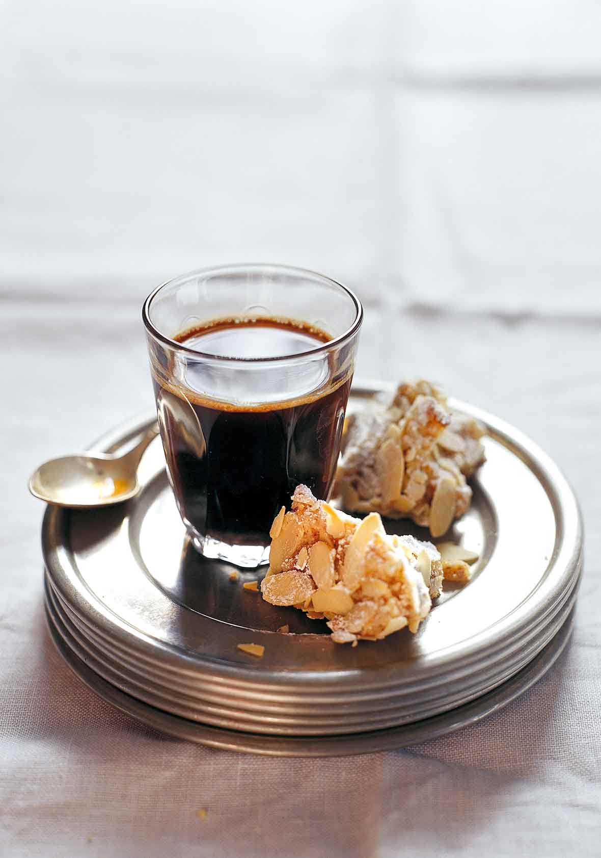 Two pieces of Rosa's almond biscotti on a stack of plates with a glass of coffee