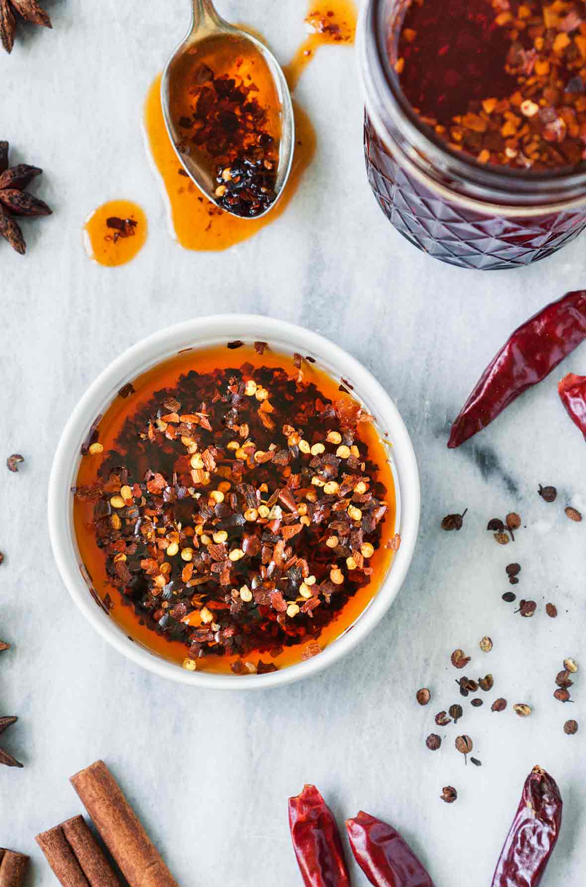 A white bowl filled with sichuan chili oil, with chiles and pepper flakes surrounding it
