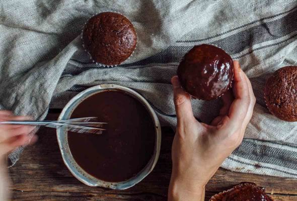 A woman's hand holding a frosted vegan gluten free cupcake and using the other hand to whisk frosting