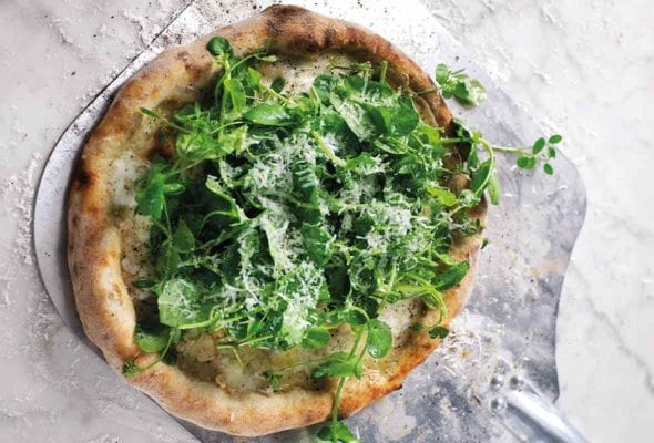 A homemade white pizza with salad, topped with Parmesan on a metal peel