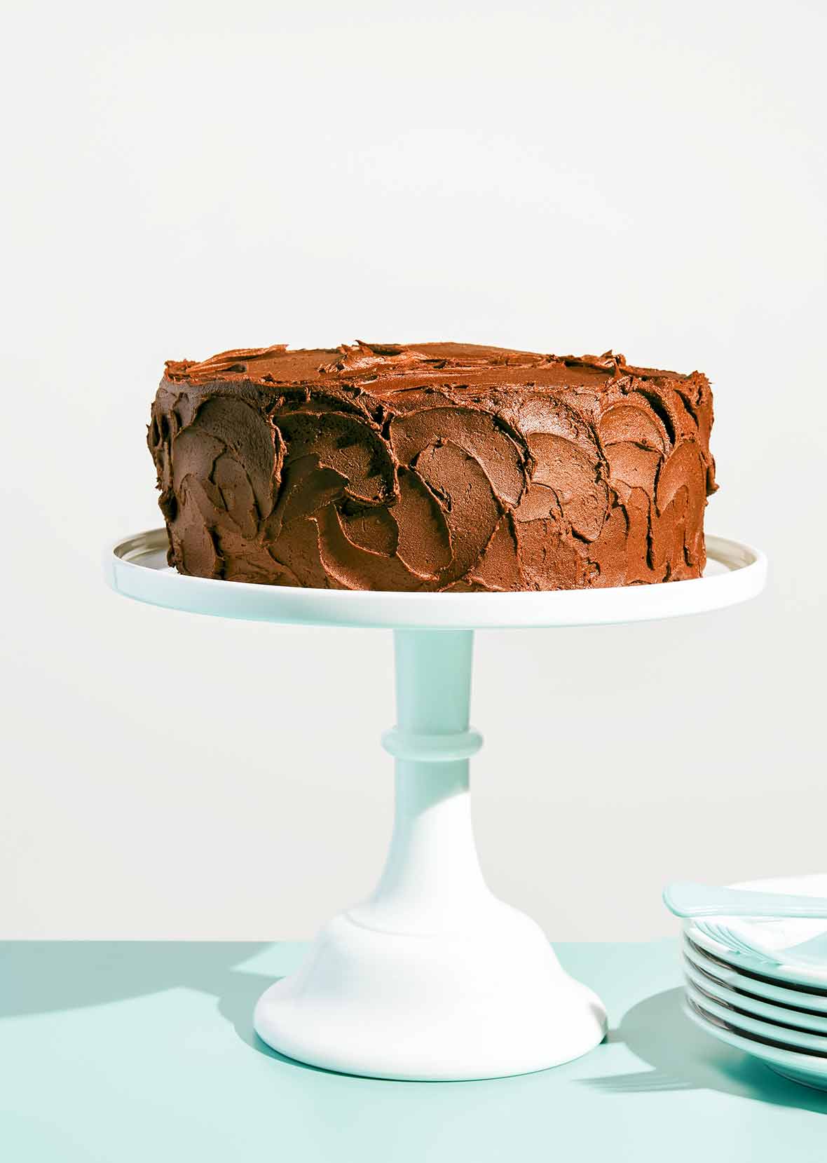 A yellow cake with chocolate frosting on a white cake stand