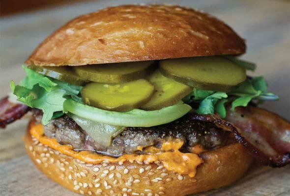 A fully loaded bacon Manchego cheese burger on a sesame bun.