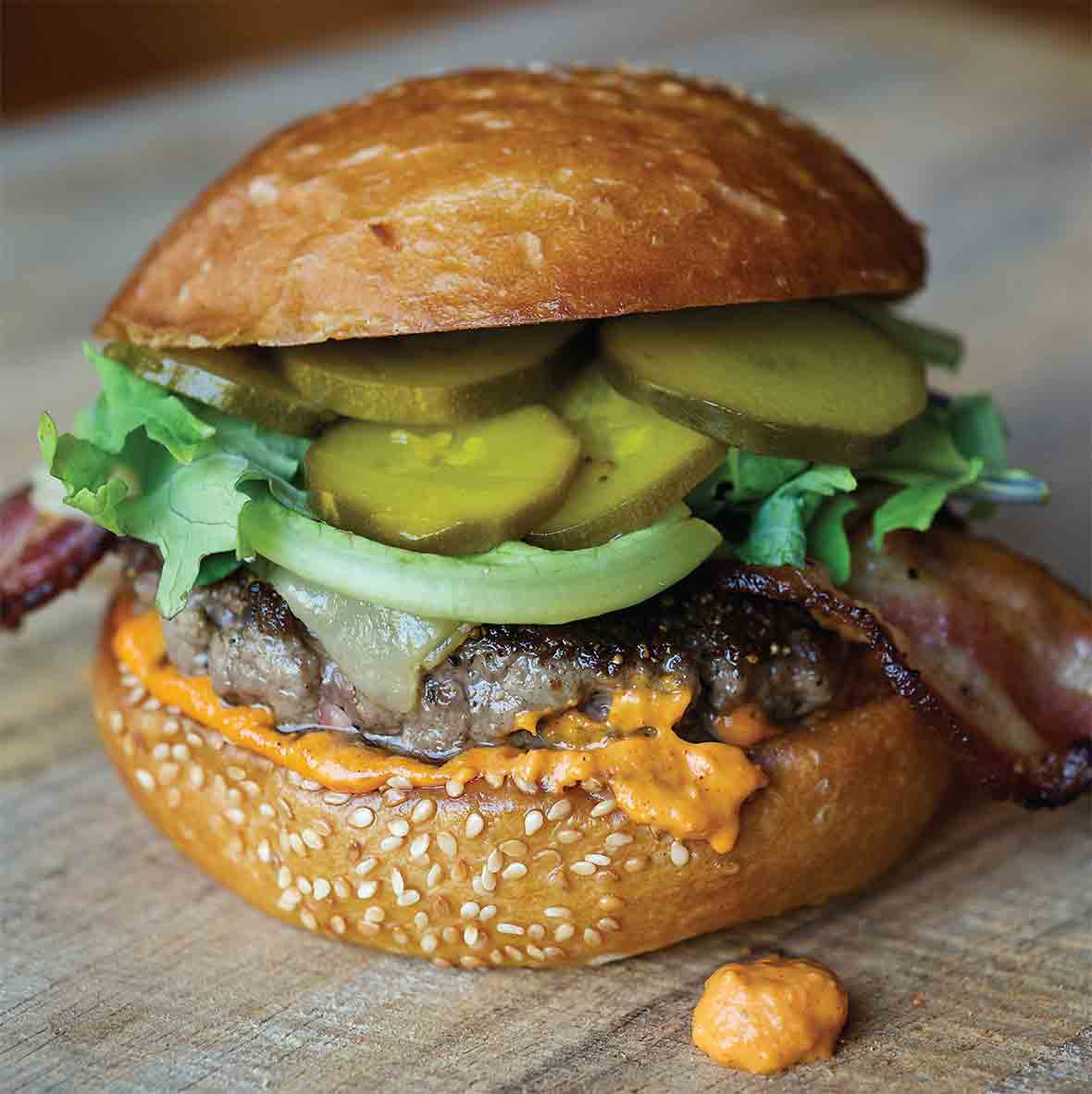 A fully loaded bacon Manchego cheese burger on a sesame bun.