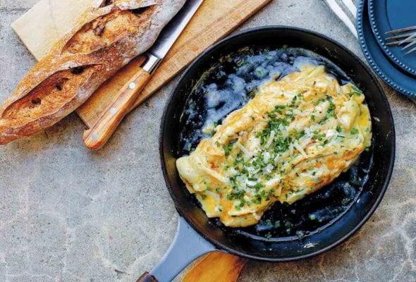 A black skillet containing a cheese omelet, topped with chives and Gruyere