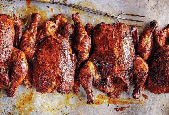 Four whole Texas smoked chickens on a baking sheet with grilling fork on the side