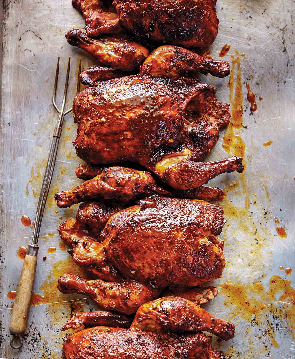 Four whole Texas smoked chickens on a baking sheet with grilling fork on the side