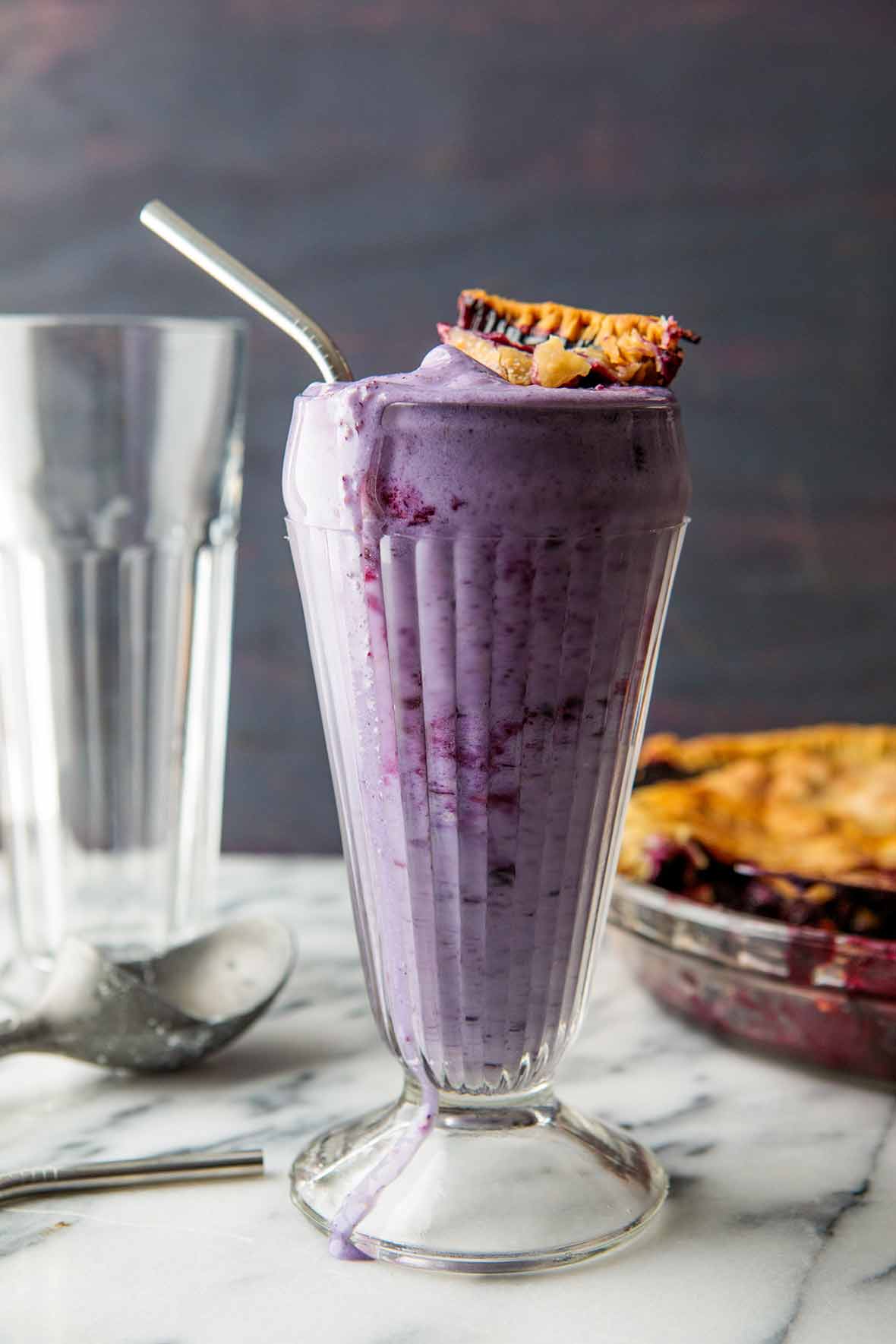 A tall glass filled with blueberry pie milkshake, topped with a piece of pie crust.