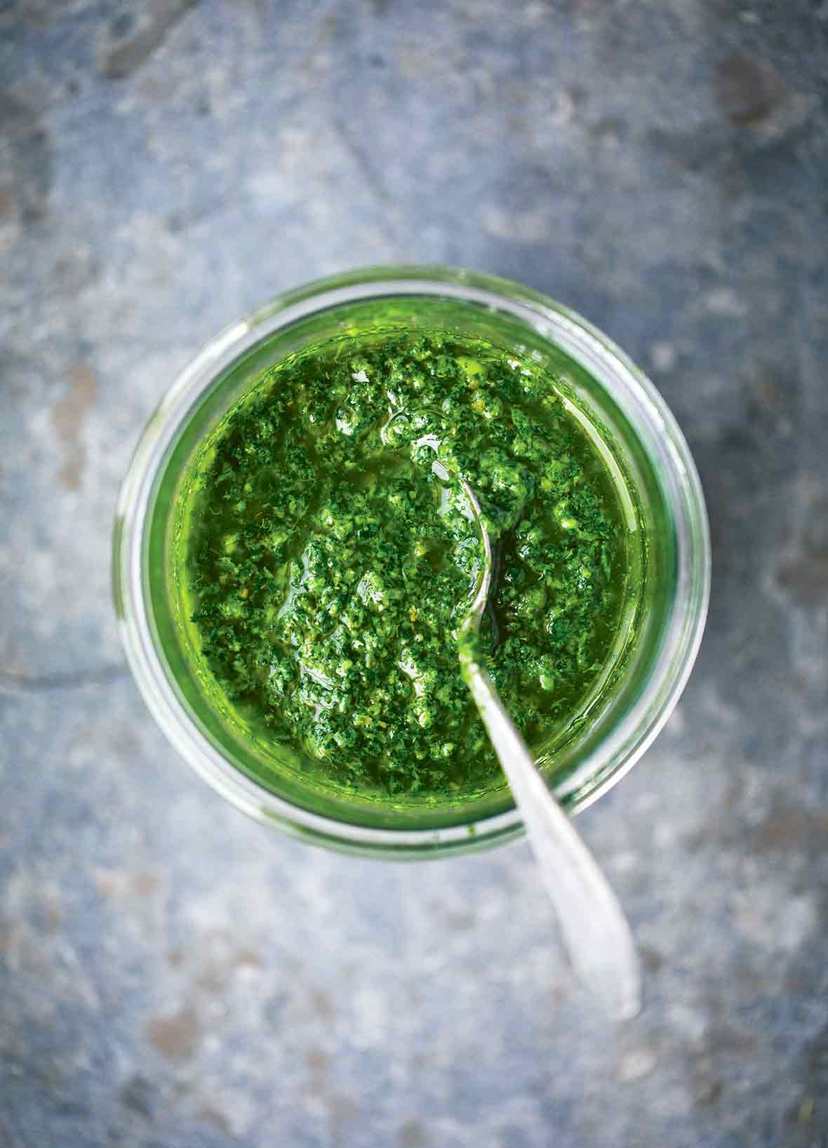 A glass jar filled with green sauce with a spoon resting inside.