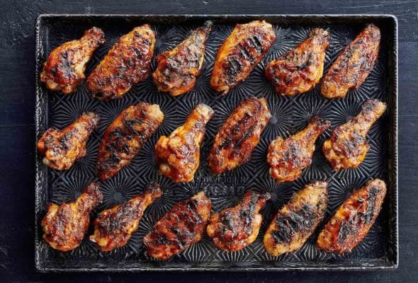 A rimmed baking sheet with 18 grilled chicken wings with maple bourbon sauce.