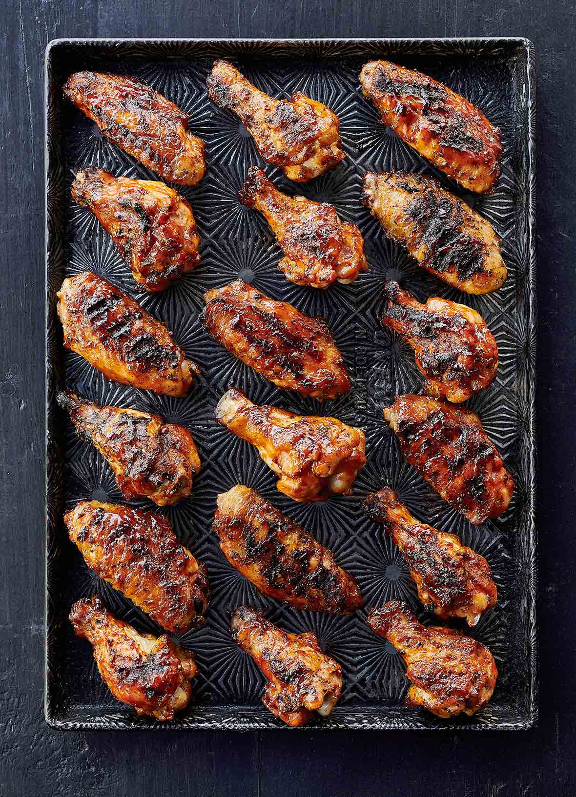 A rimmed baking sheet with 18 grilled chicken wings with maple bourbon sauce.