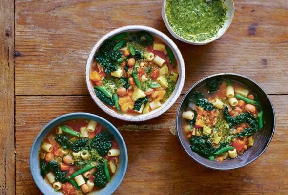 Three bowls of minestrone soup and a small bowl of pesto.