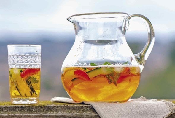 A pitcher of Pimm's cup, with a half-filled glass and a vase of flowers on either side of it.