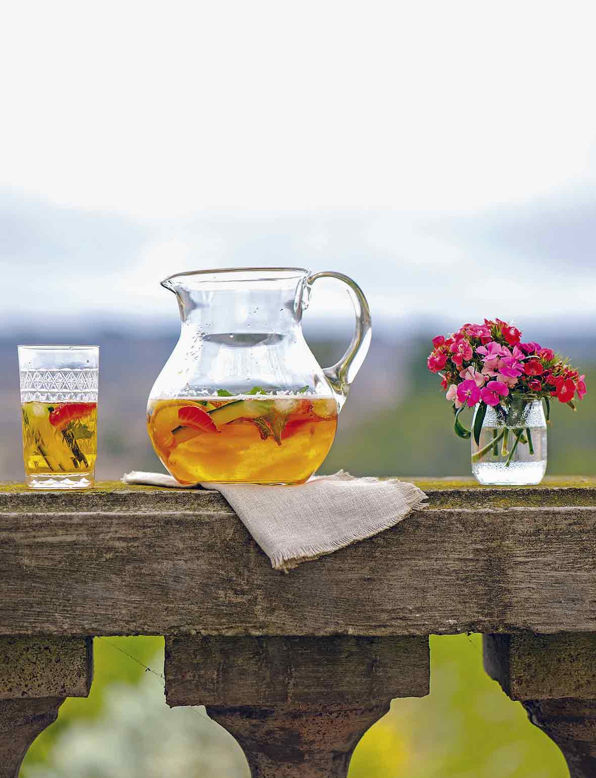 A pitcher of Pimm's cup, with a half-filled glass and a vase of flowers on either side of it.