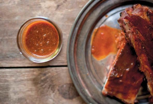 A platter of ribs covered with Texas-style barbecue sauce, and a glass of extra sauce on the side.