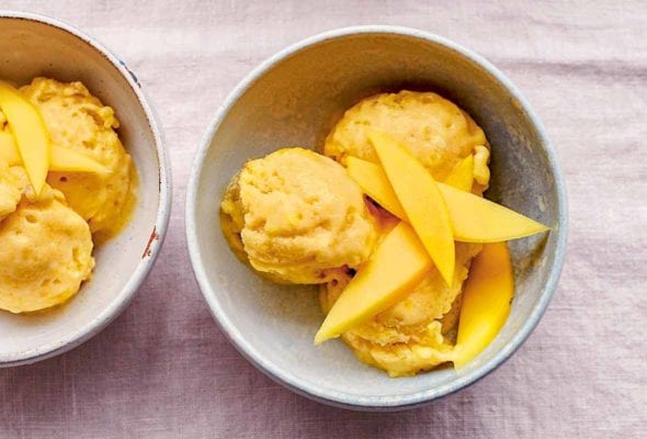 Three bowls of vegan mango ice cream topped with mango slices.