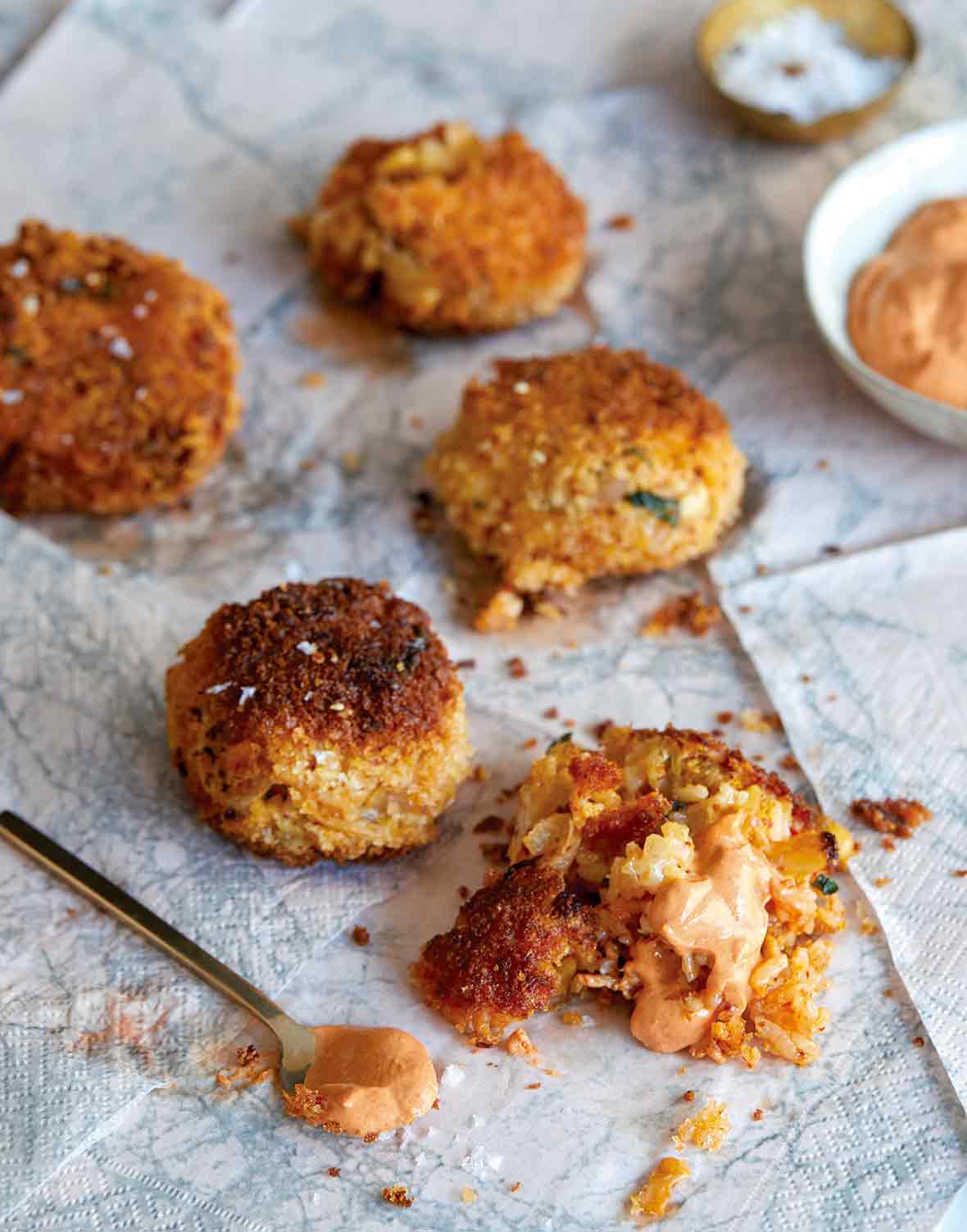 Four deep-fried kimchi arancini on paper towels with a bowl of gochujang sour cream in the background.