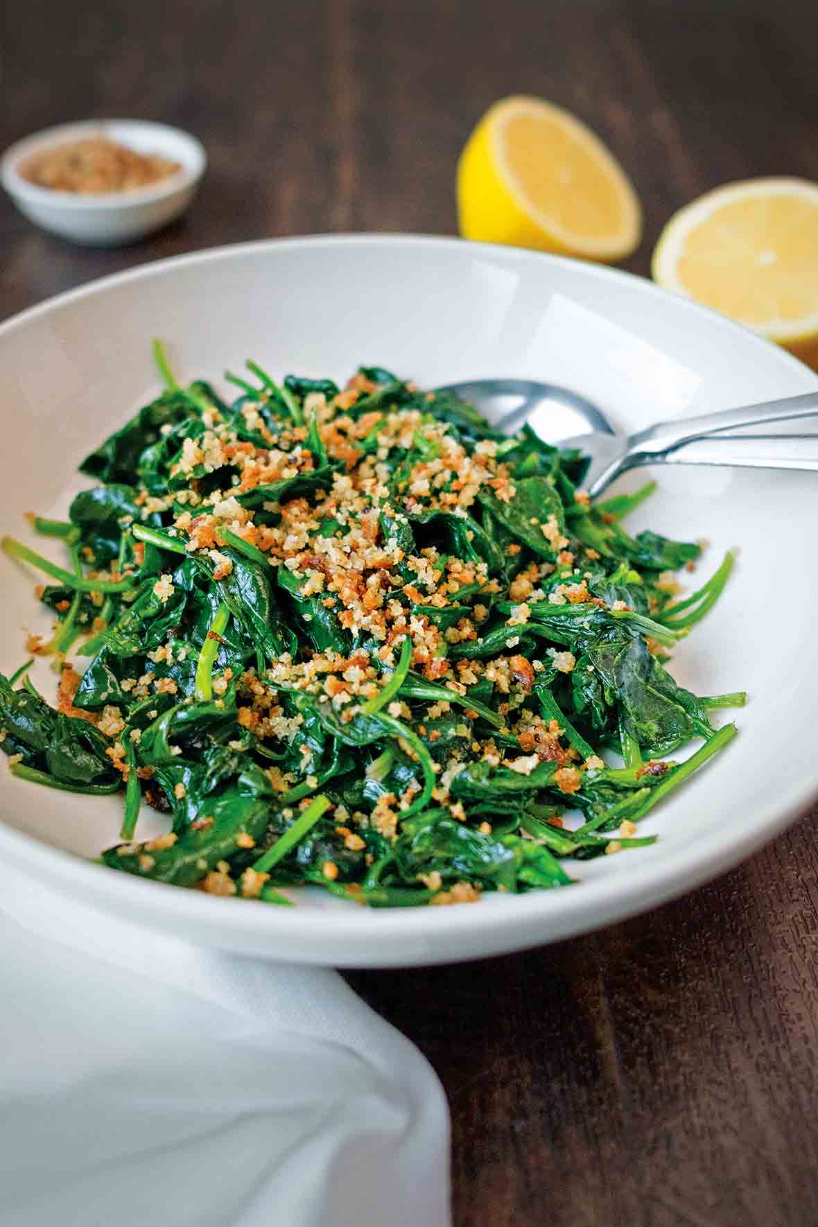 A white serving bowl filled with sauteed spinach and bread crumbs.
