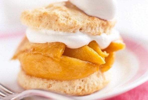 A spiced peach shortcake on a white plate with spiced peaches layered between two biscuit halves and topped with whipped cream.