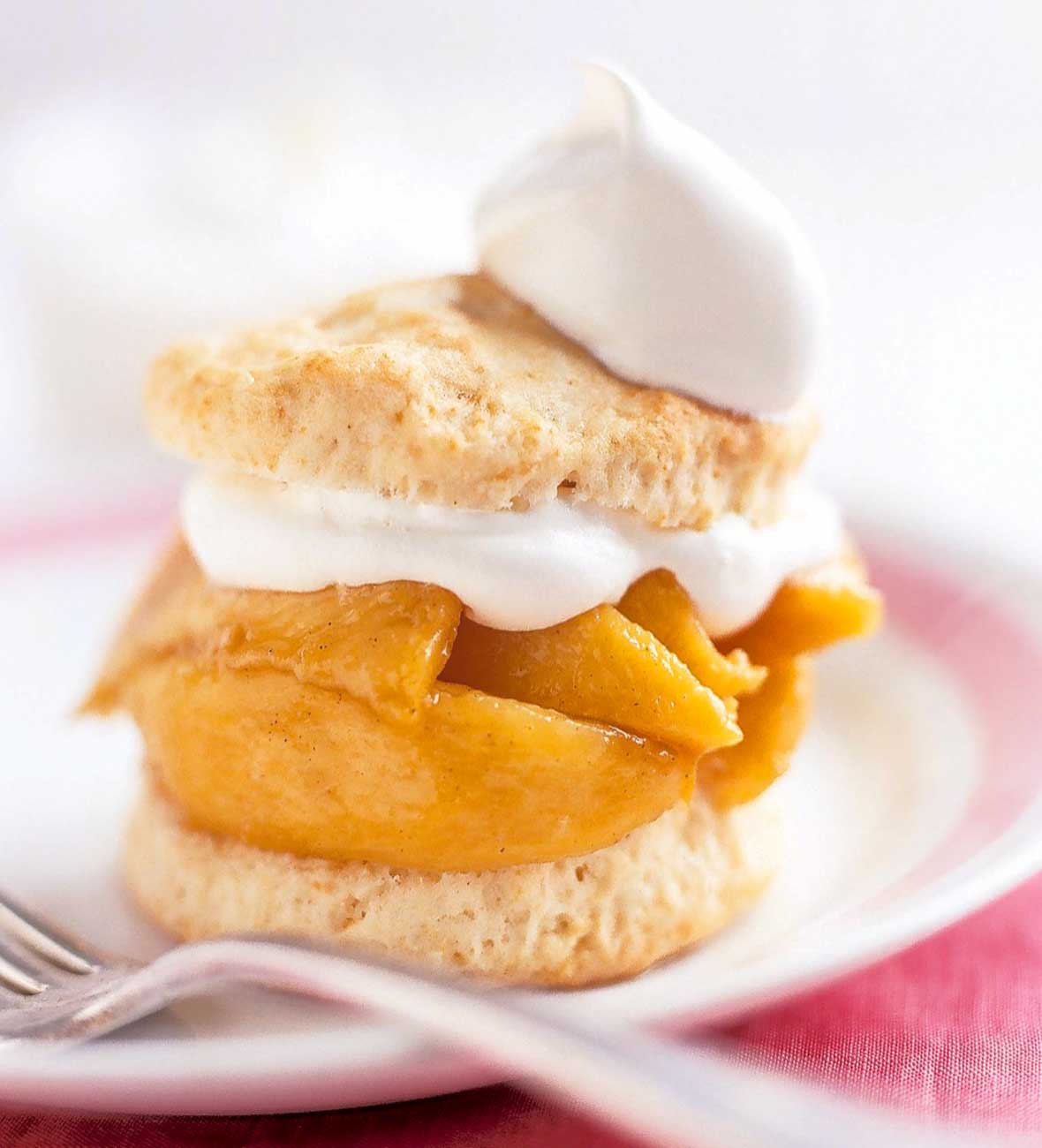 A spiced peach shortcake on a white plate with spiced peaches layered between two biscuit halves and topped with whipped cream.