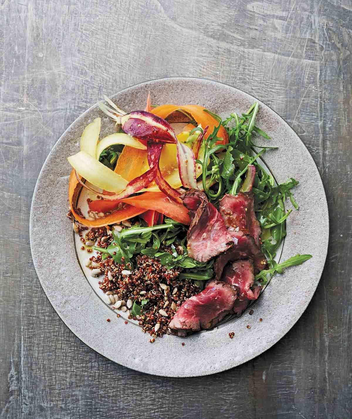 A grey plate topped with steak and quinoa salad with shaved carrots and mustard vinaigrette.