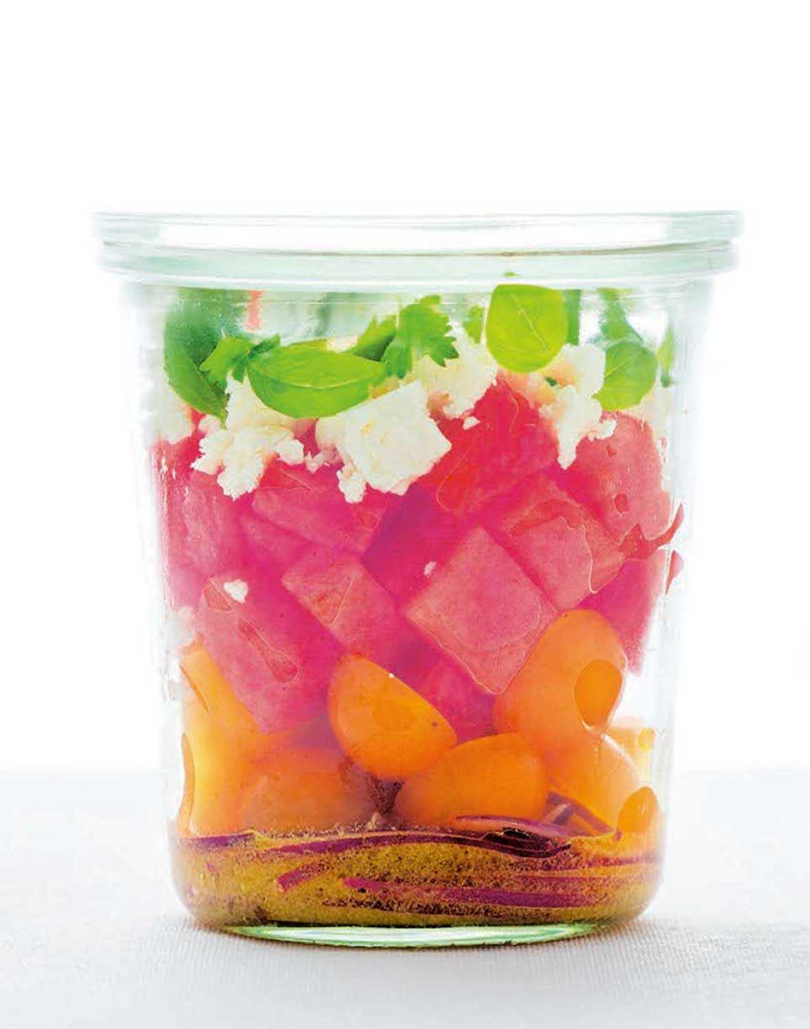 A jar of layered watermelon tomato feta salad with red wine vinaigrette on the bottom.