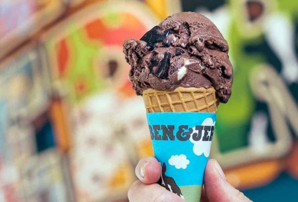 A hand holding a scoop of Ben & Jerry New York super fudge chunk in a sugar cone.