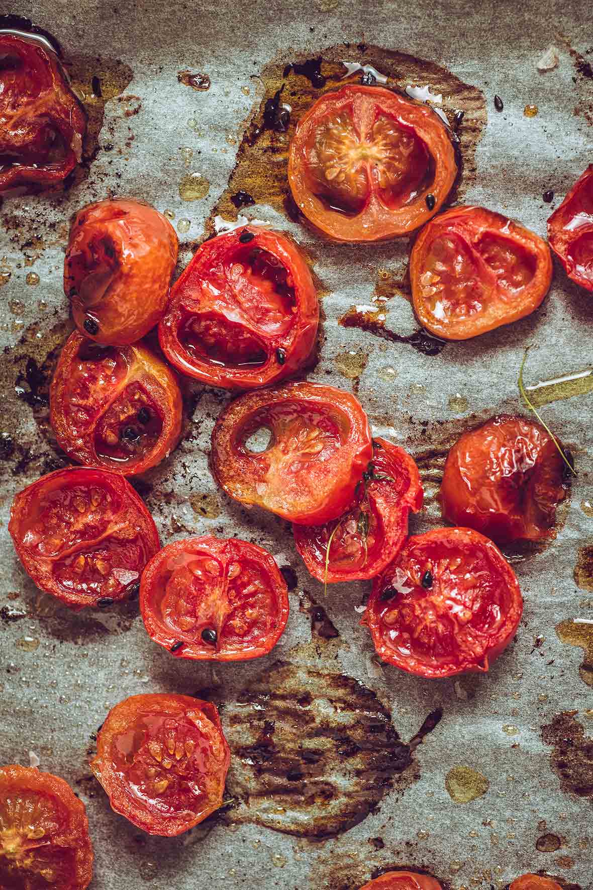 Halved slow roasted tomatoes on a piece of parchment with drops of oil and flakes of salt.