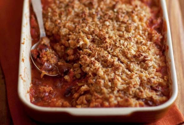A rectangular casserole dish filled with spicy tomato crumble, and a spoon resting in it.