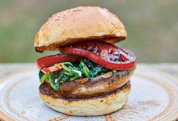 A spinach tomato mushroom burger between two toasted bun halves on a brown plate.