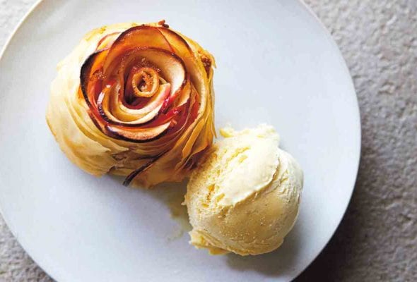 An apple rose tart, shaped to look like a rose with a scoop of ice cream beside it on a white plate.