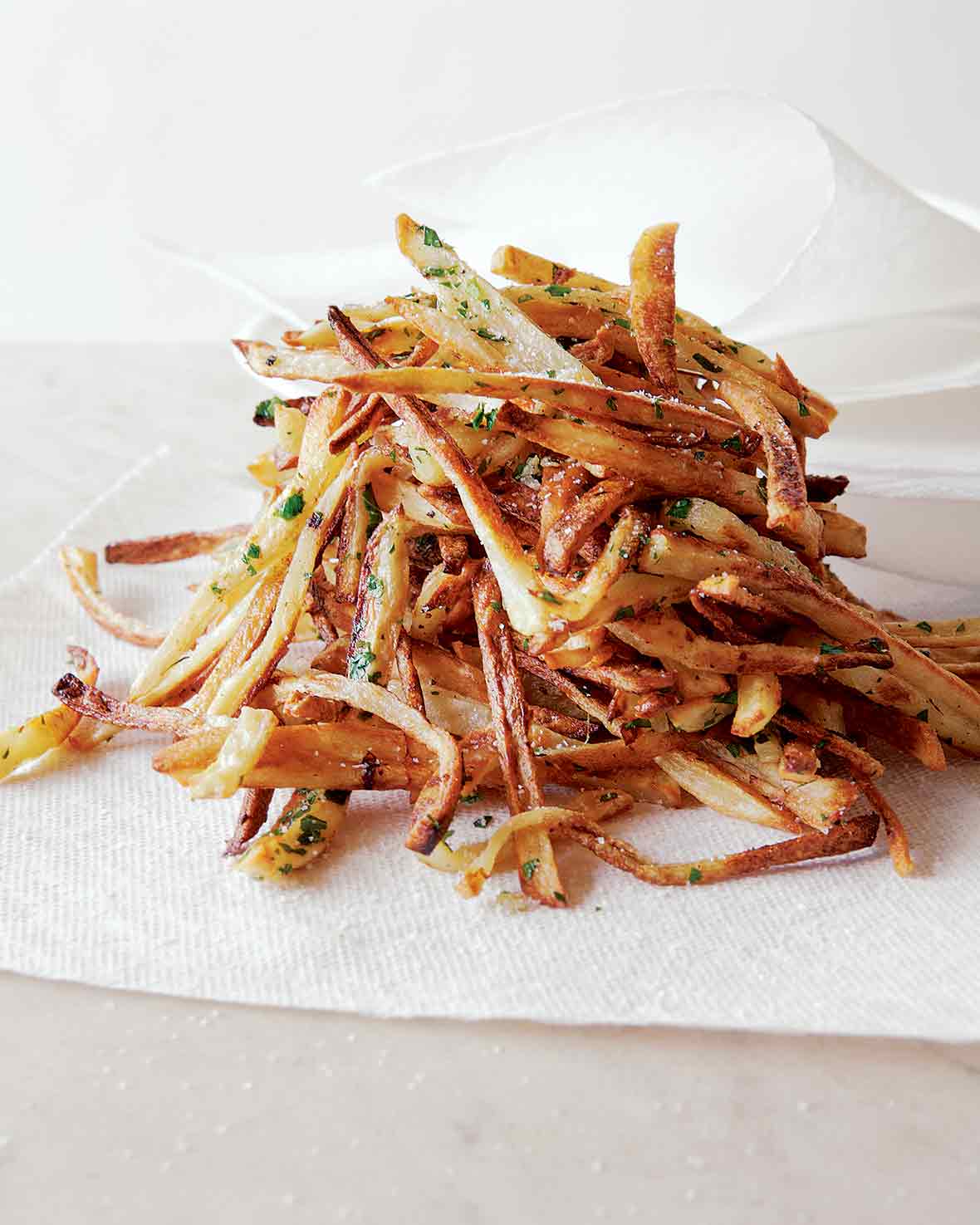 A pile of baked french fries, sprinkled with salt and fresh parsley on a paper towel.
