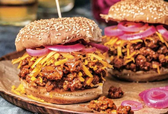 Two bourbon sloppy joes on sesame buns, topped with shredded Cheddar cheese, and pickled red onion.