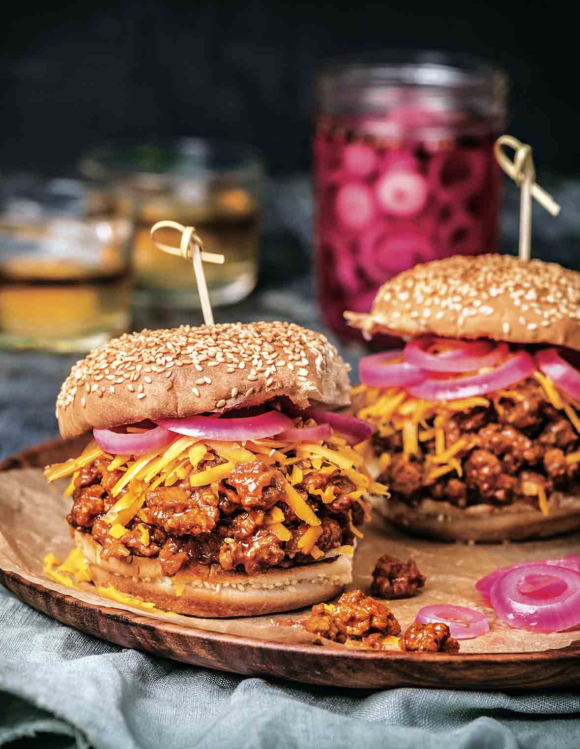 Two bourbon sloppy joes on sesame buns, topped with shredded Cheddar cheese, and pickled red onion.