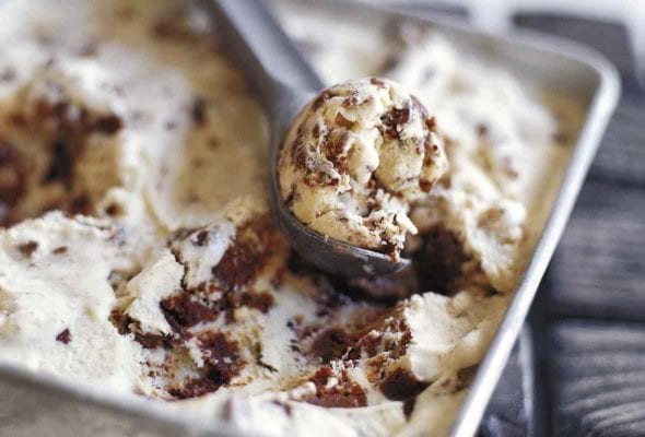 A square metal dish filled with brownie ice cream and a metal ice cream scoop removing a scoop from the dish.