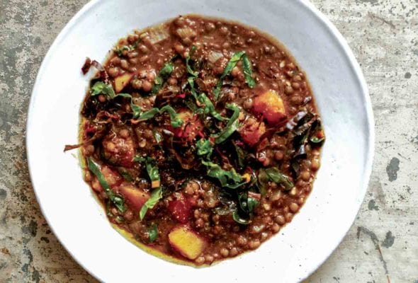 A white bowl of French lentil soup, topped with ribbons of chard.