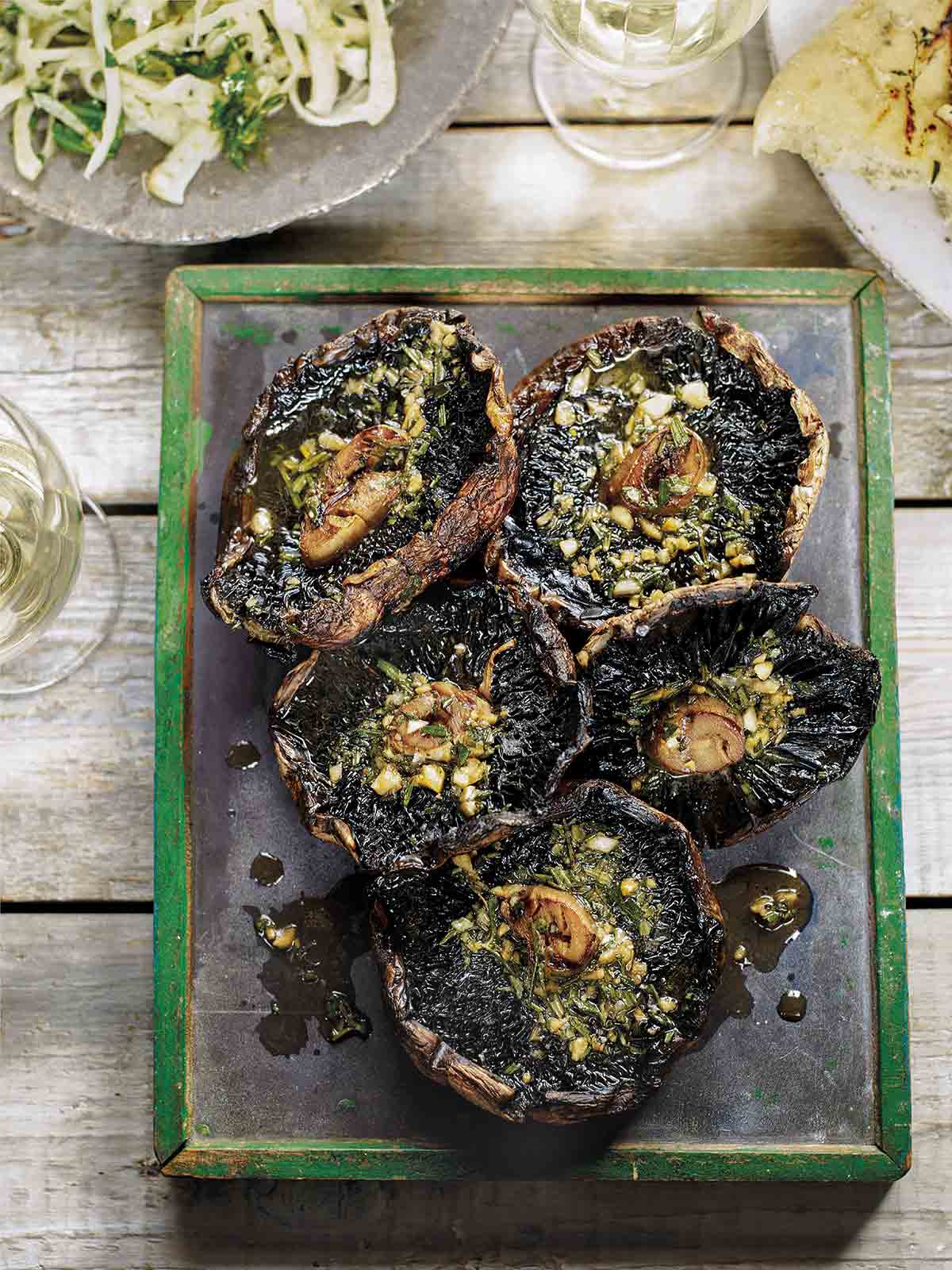 A metal platter holding five grilled portobello mushrooms, topped with garlic rosemary butter.