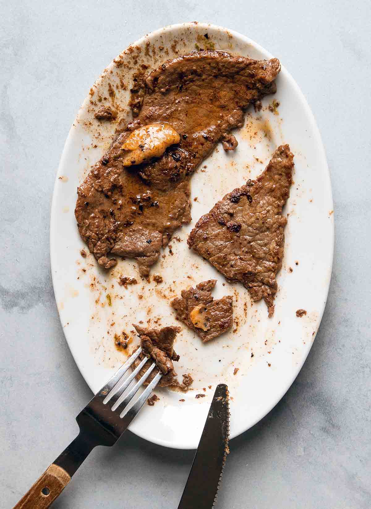 Two pieces of steak with chile-lime butter on an oval plate with a fork and knife cutting the steak.