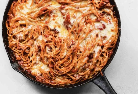 A cheesy baked spaghetti casserole in a cast-iron skillet.