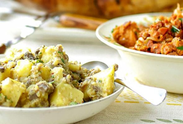 A Portuguese roast turkey with two stuffings in white bowls with a spoon resting in one of the bowls.