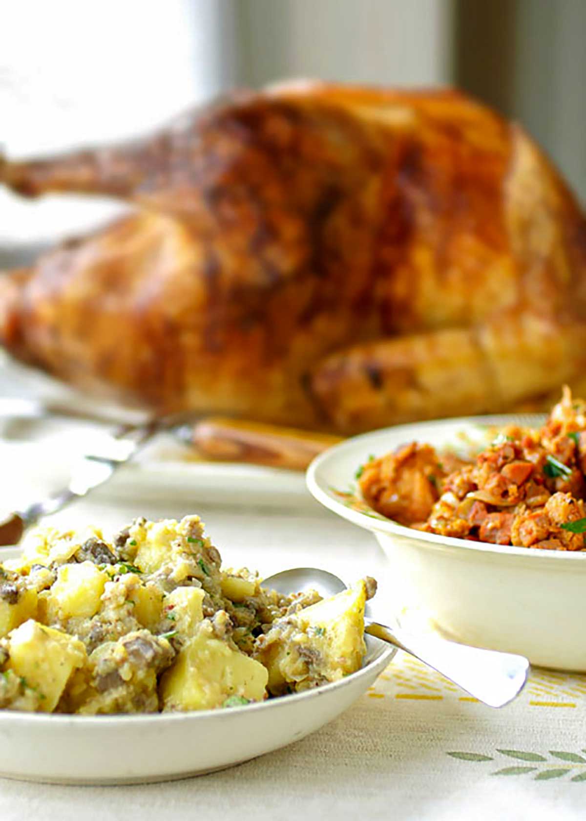 A Portuguese roast turkey with two stuffings in white bowls with a spoon resting in one of the bowls.
