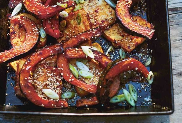 A black rectangular serving dish filled with slices of roasted squash with chile and honey, slices of roasted tofu, scallions, squeezed lime halves, and sesame seeds.