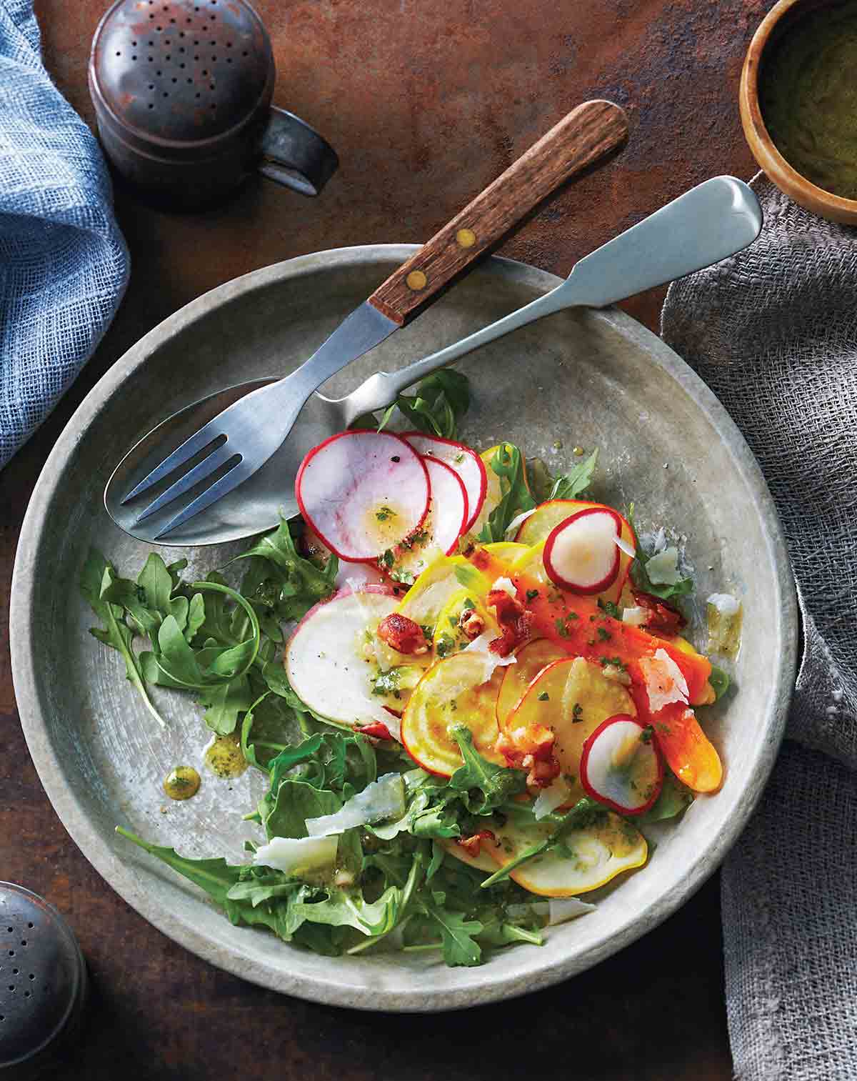 Shaved root vegetable salad in a grey bowl with a fork and spoon resting inside.
