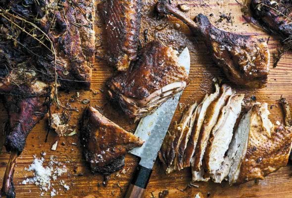 A Texas style smoked turkey cut into breast and leg pieces on a cutting board with a knife.